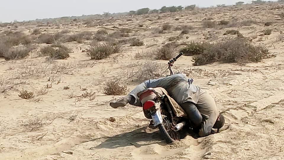 A motorcycle fuel transporter, lies beside his fallen bike after getting stuck in deep sand along a desert stretch near Kuntani Hor 