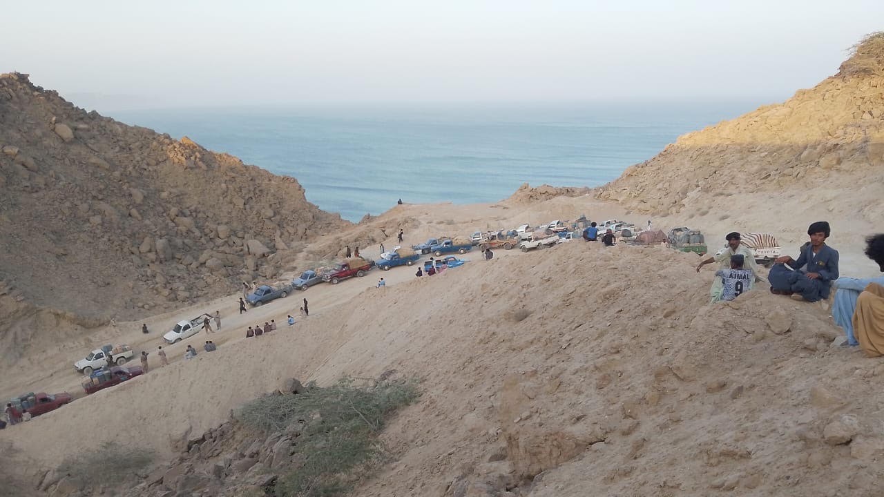 Workers rest on a hillside as pickups line the rough coastal track leading from Kuntani Hor, to transport Iranian fuel to depots and other areas across Balochistan 