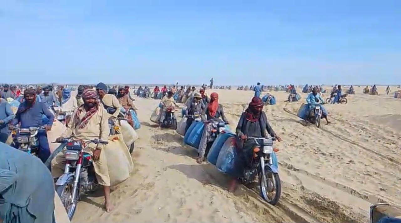 Motorcycle fuel transporters cross the sandy desert stretch near Kuntani Hor, dragging their feet to steady bikes loaded heavily with flammable fuel 