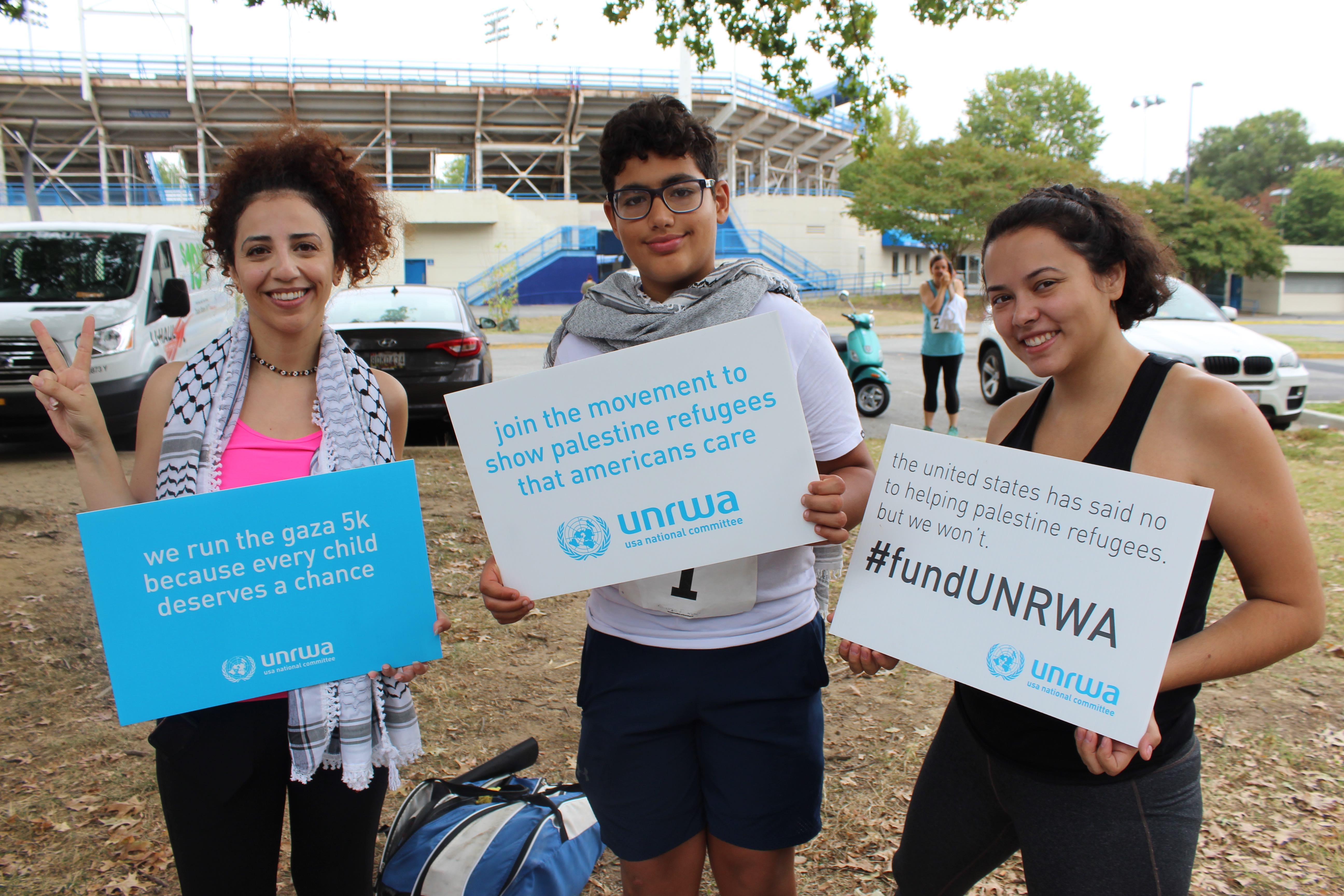 Three participants in UNRWA USA's race hold up signs in support of the agency (MEE/Sheren Khalel) 