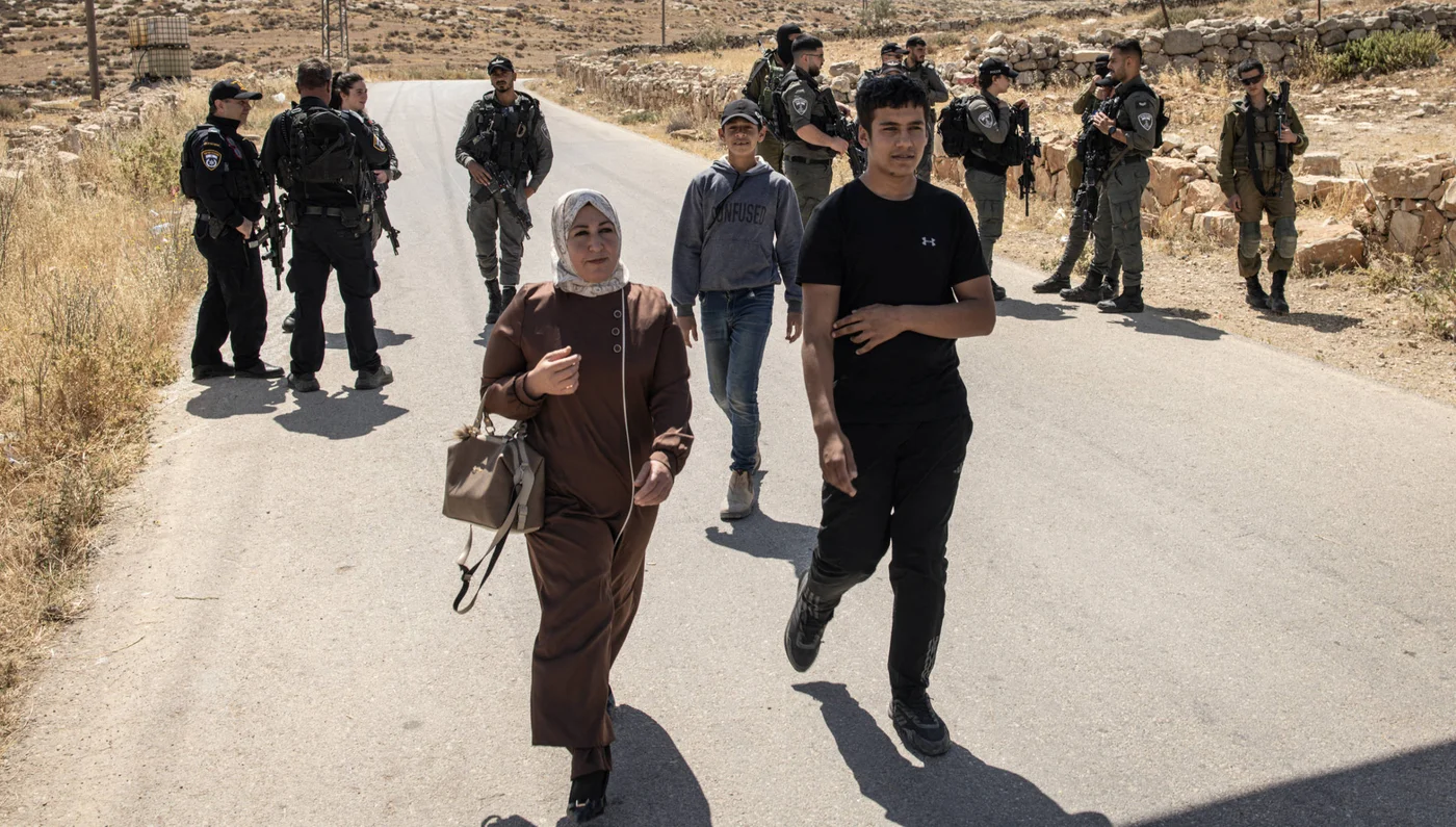 People walk past Israeli security forces as they block the entrance to the village of al-Tuwani in the Masafer Yatta area in occupied West Bank on 2 June 2025 (AFP)