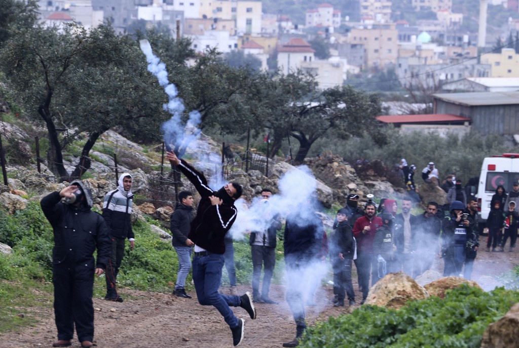 A demonstrator returns a tear gas canister towards Israeli forces, as Palestinians protest Israeli outposts on their lands east of Nablus on 18 March 2022 (AFP)