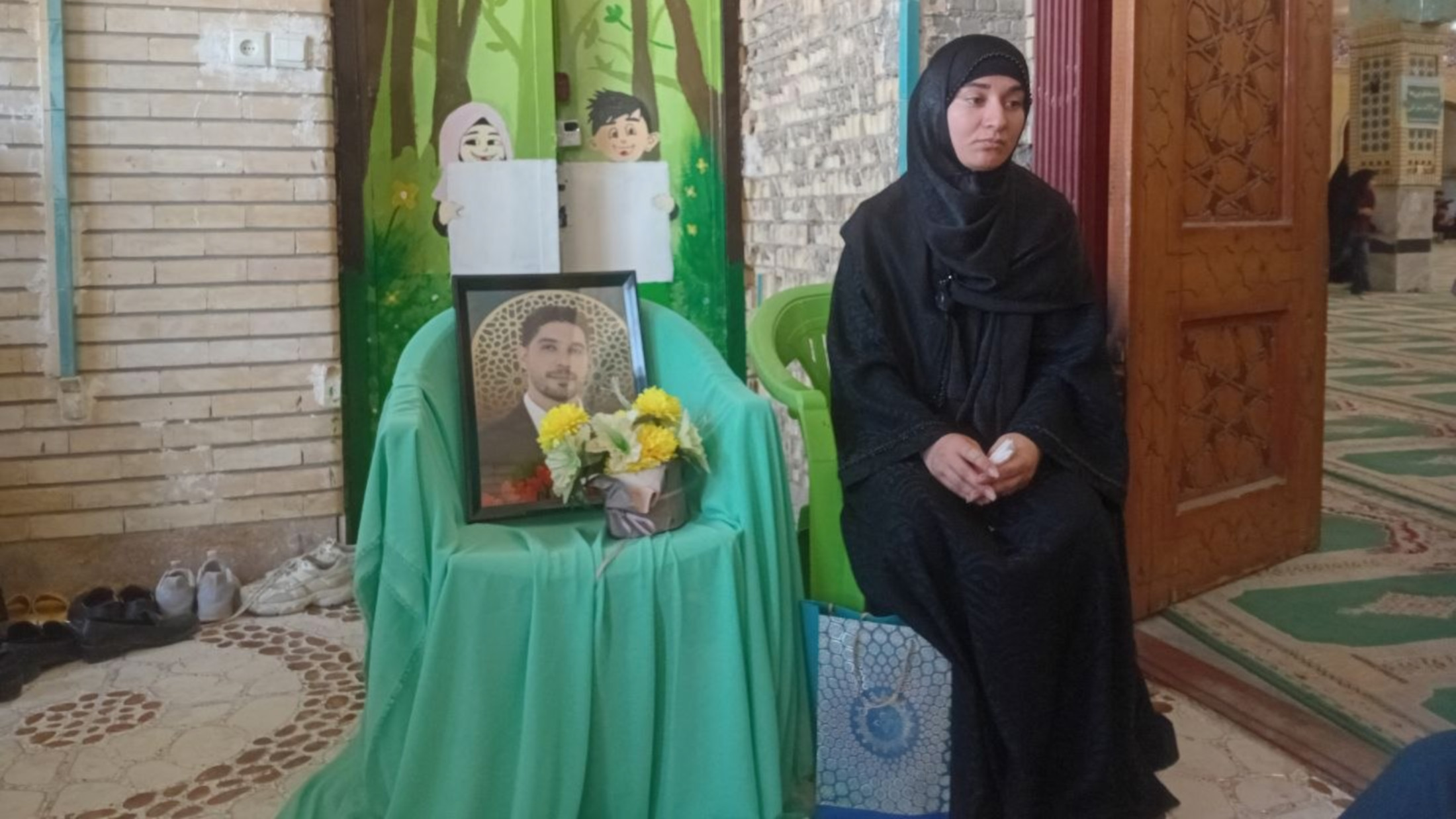 The widow of football coach Mahmoud Najafi sits beside his portrait at a condolence gathering after he was killed in US strikes in Lamerd (Julia Kassem/MEE)