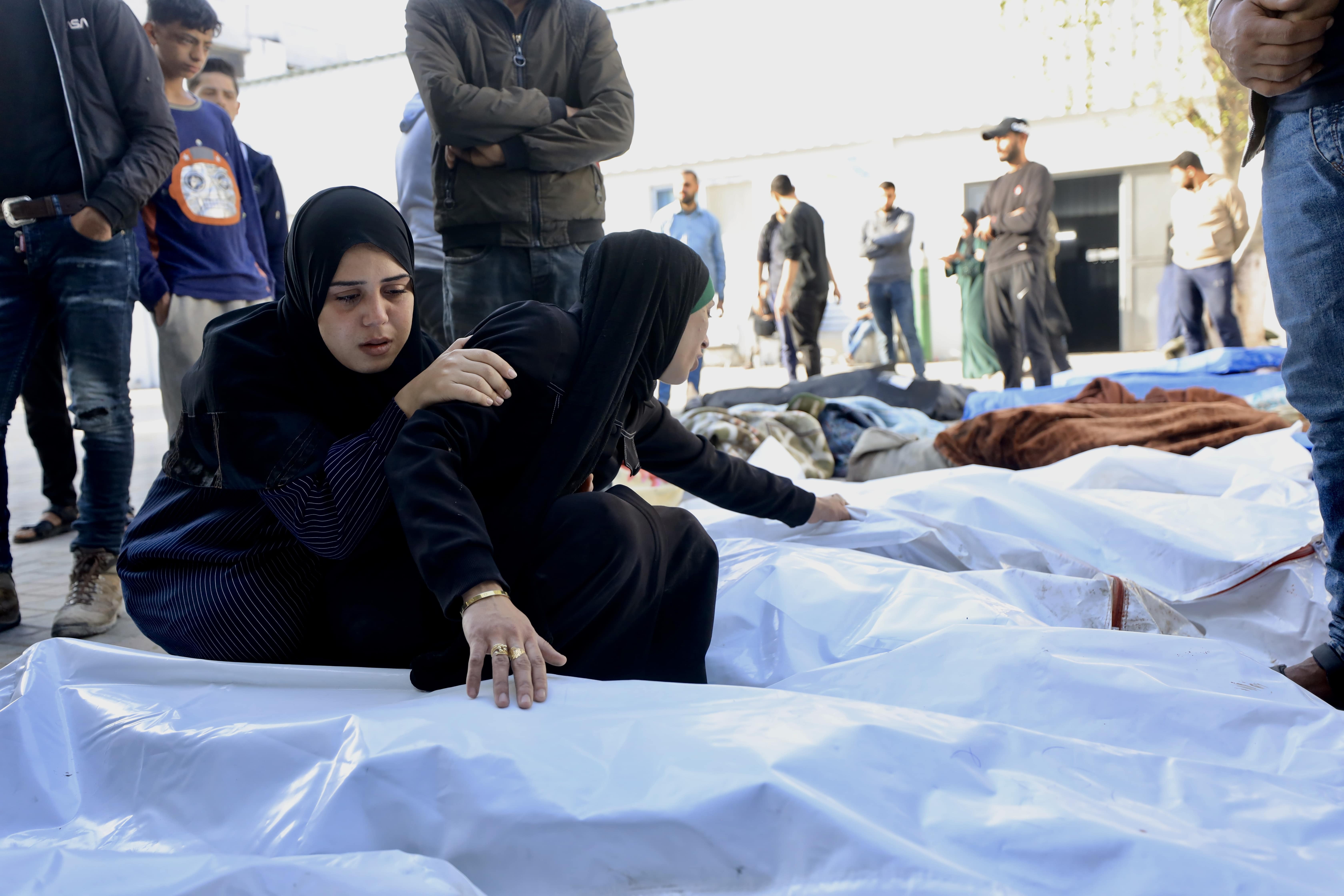Women lie next to bodies draped in shrouds who were killed in Israeli attacks across the Gaza Strip