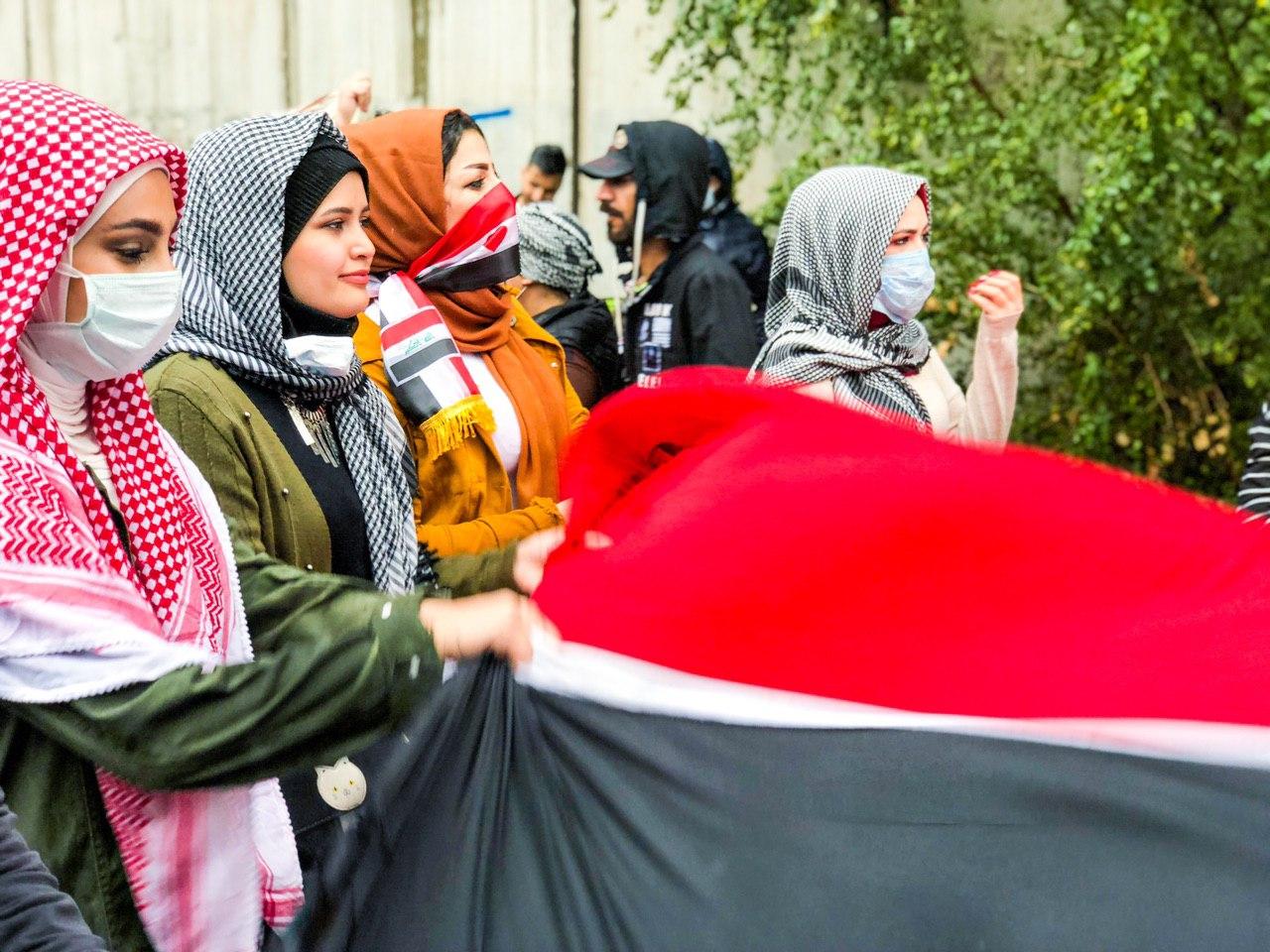 Women wearing surgical masks wave the Iraqi flag at a Baghdad protest